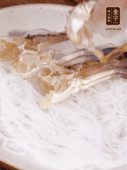 盤底墊上粉絲，擺上梭子蟹、火腿片，撒姜粒，淋上蒸魚豉油、花雕酒調(diào)味腌制15分鐘